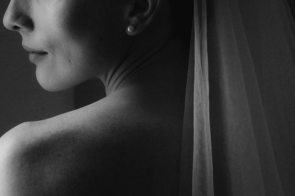 Elegant black and white portrait of bride showing bare back with veil and pearl earring on wedding day.