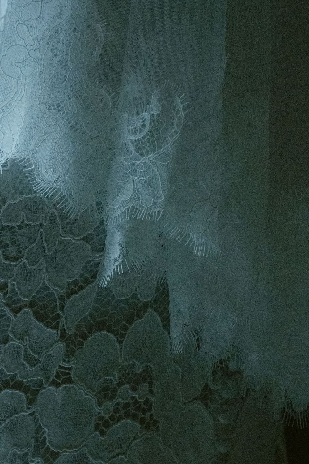 Close-up of delicate teal lace fabric with intricate floral and botanical embroidery patterns.