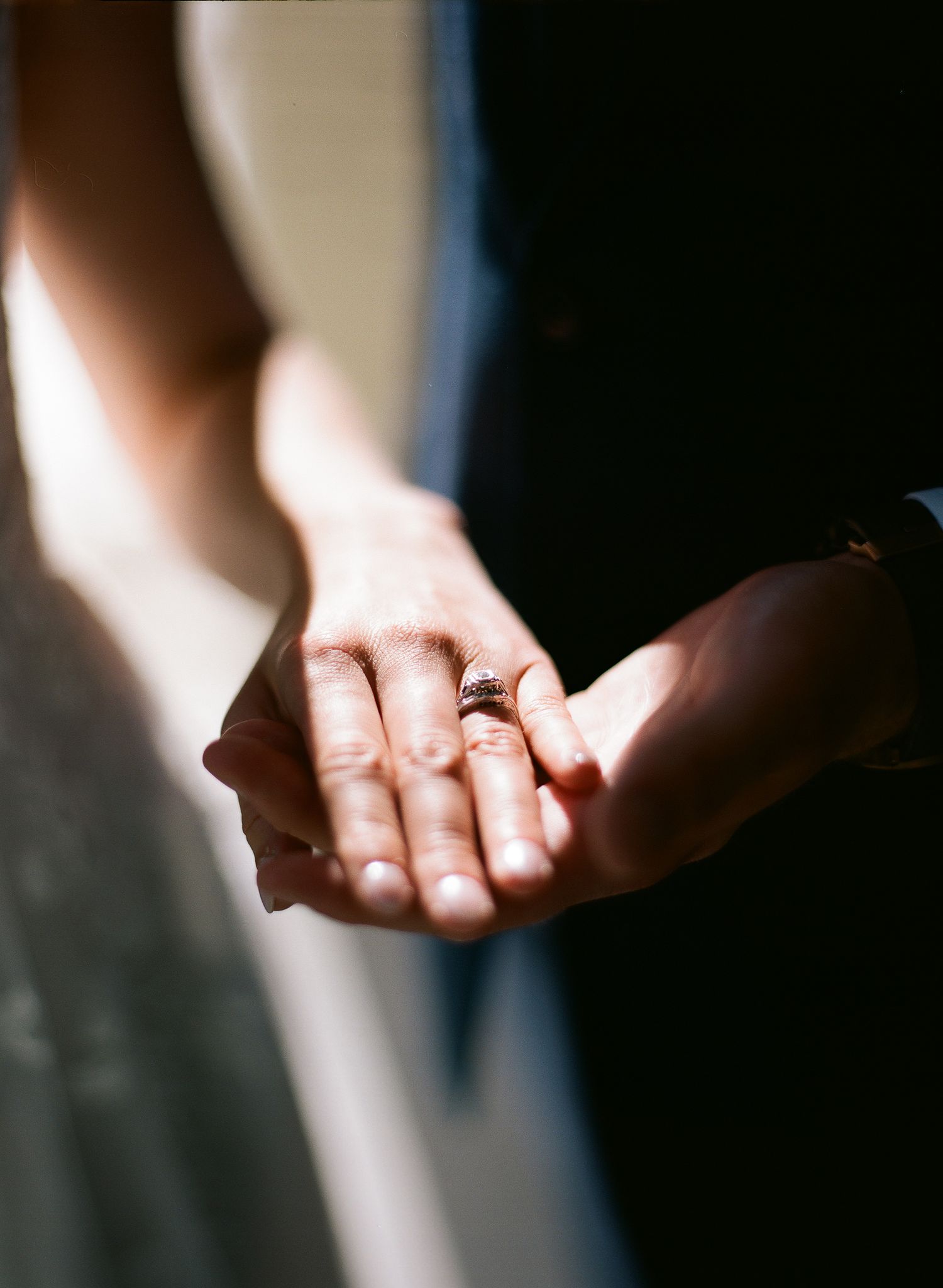 Close-up of two hands gently touching, with a diamond engagement ring visible on the woman's finger.