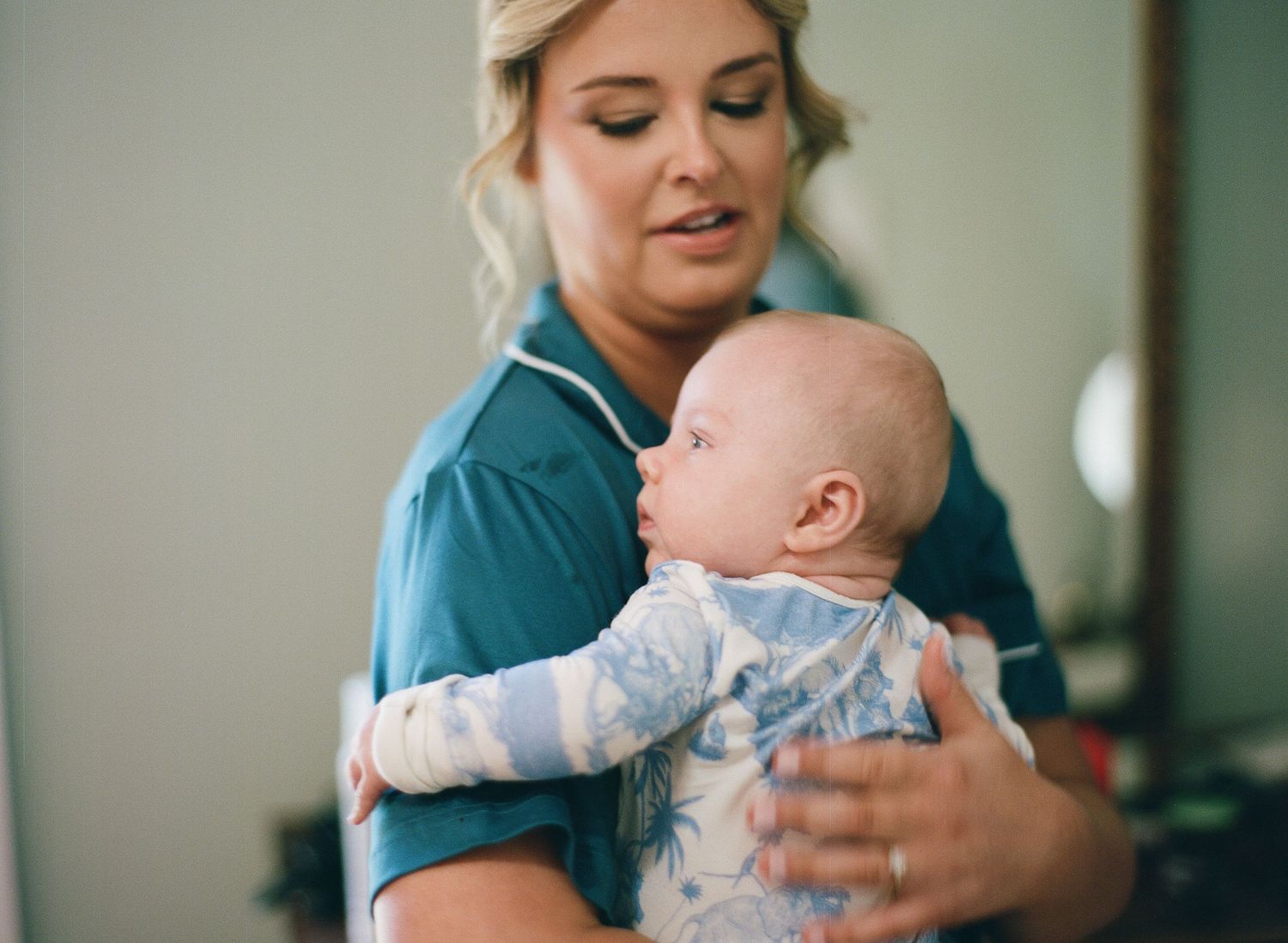 A nurse in teal scrubs gently holds a baby in a light blue outfit, providing attentive infant care.