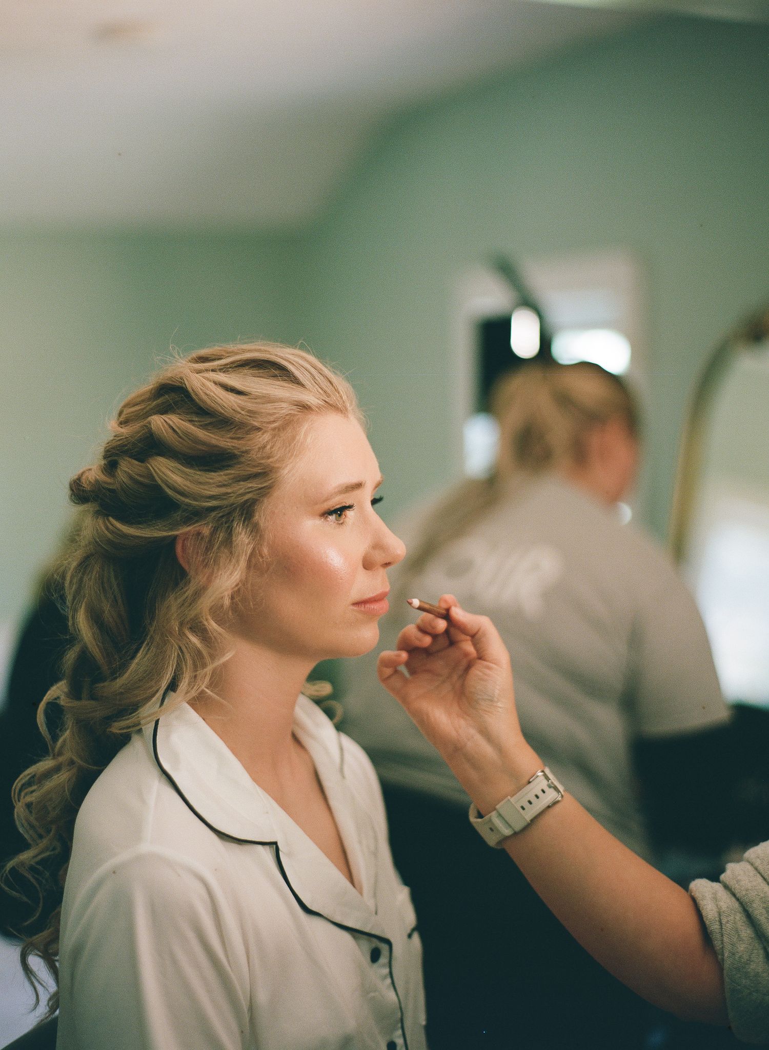 Bride getting makeup applied by artist, elegant updo hairstyle, soft natural look, wedding preparation scene.