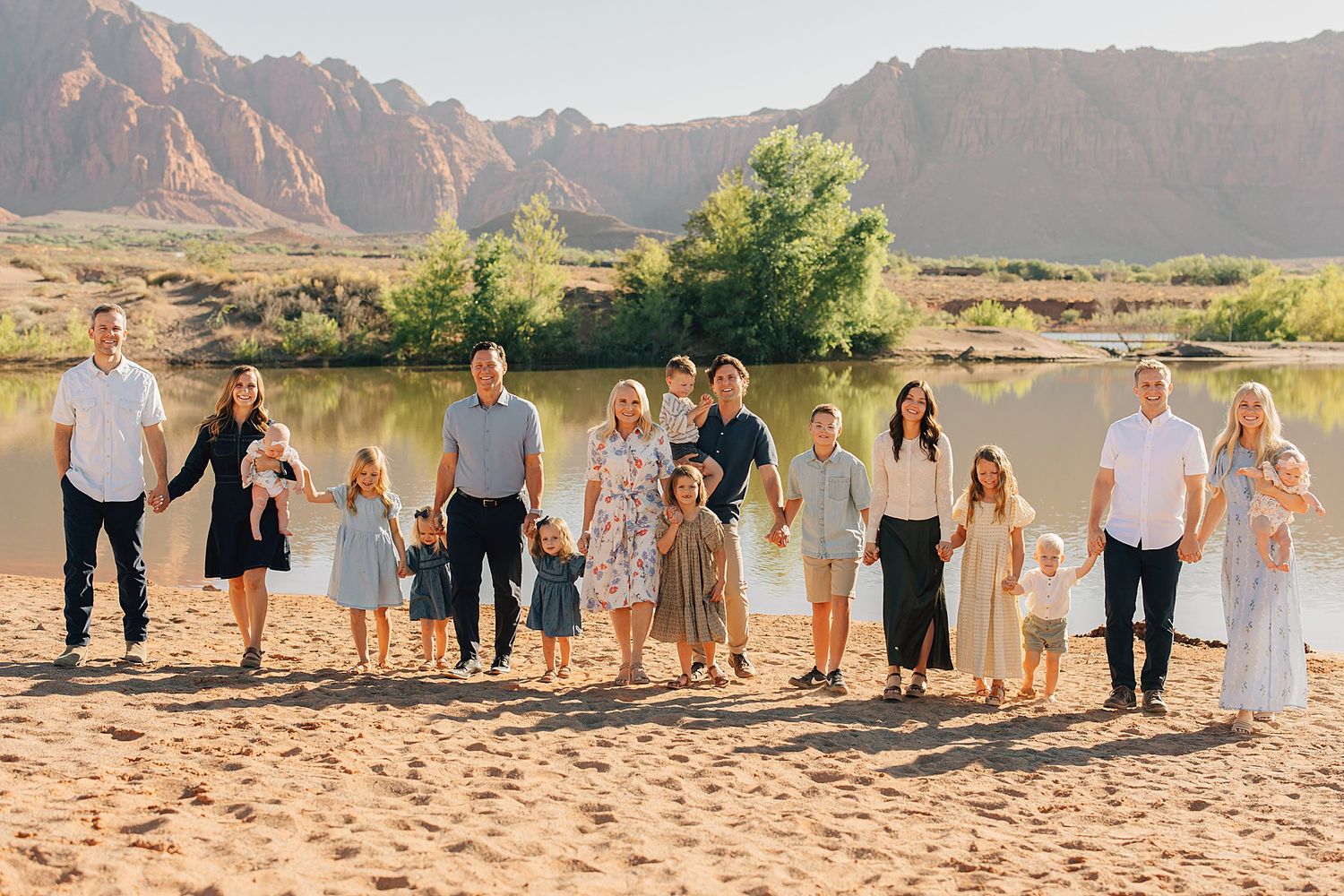 Large family group portrait on sandy beach with red rock mountains and river in background on sunny day.