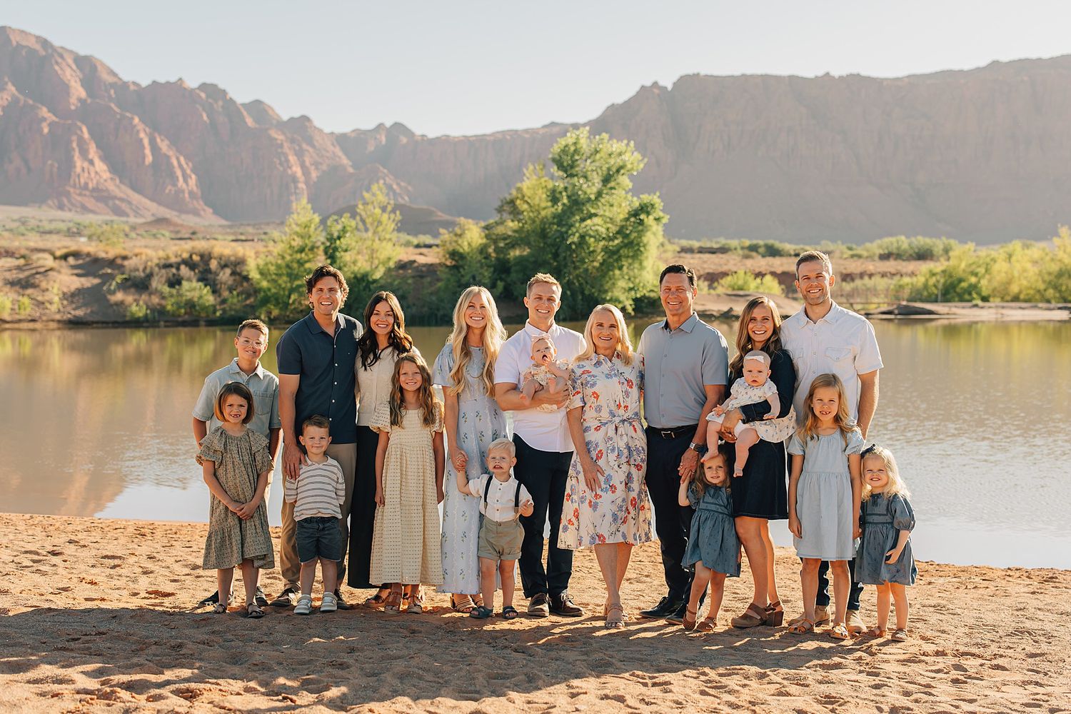 Large family group portrait outdoors near a river with red rock mountains in the background on a sunny day.