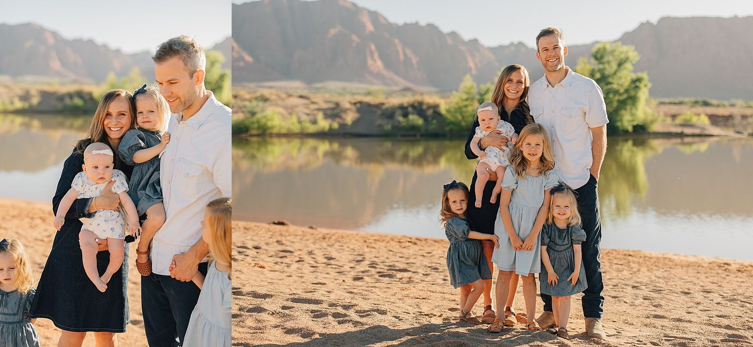 Family portrait session on sandy riverbank with mountains, parents holding babies and children posing in coordinated outfits.