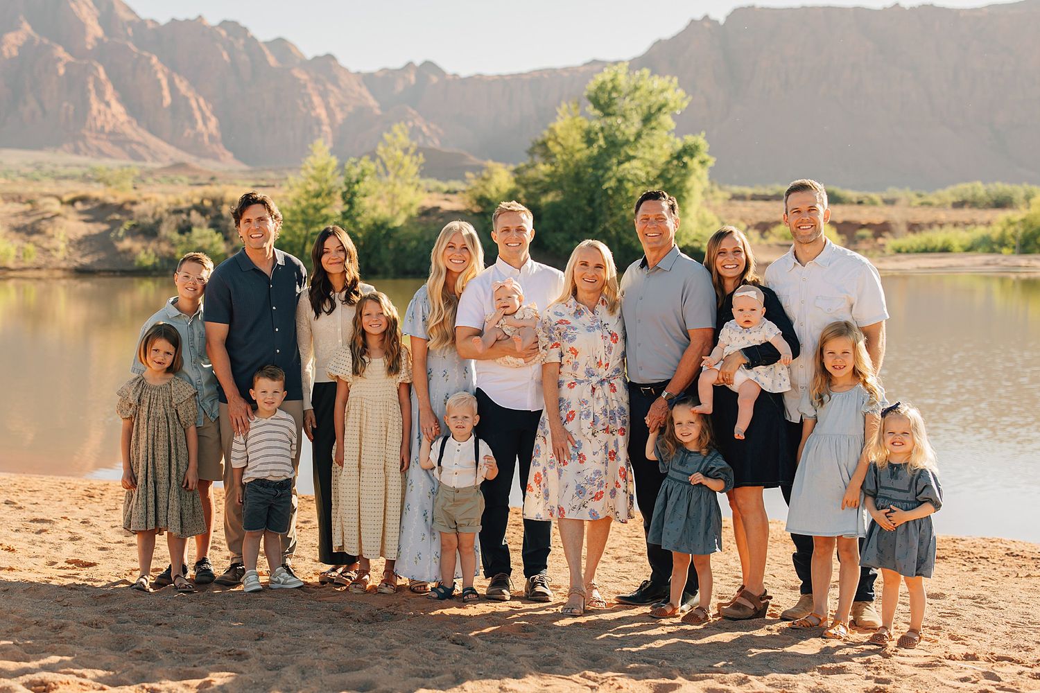 Large family group portrait outdoors near a river with red rock mountains in the background on a sunny day.