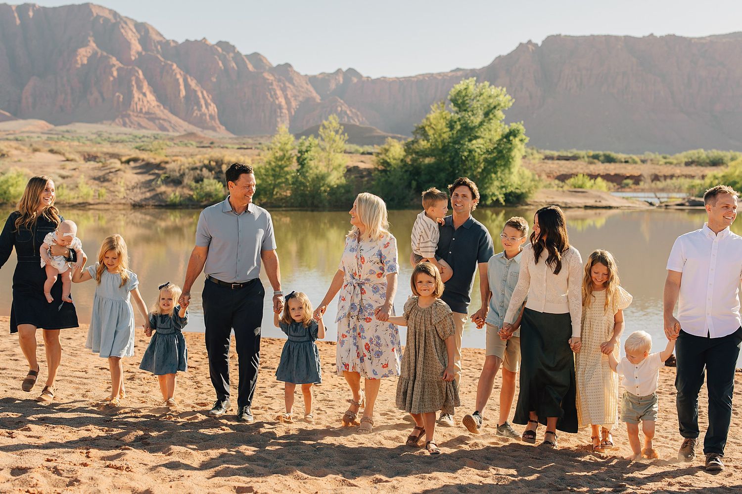 Large family group photo outdoors near a river with red rock mountains in the background on a sunny day.
