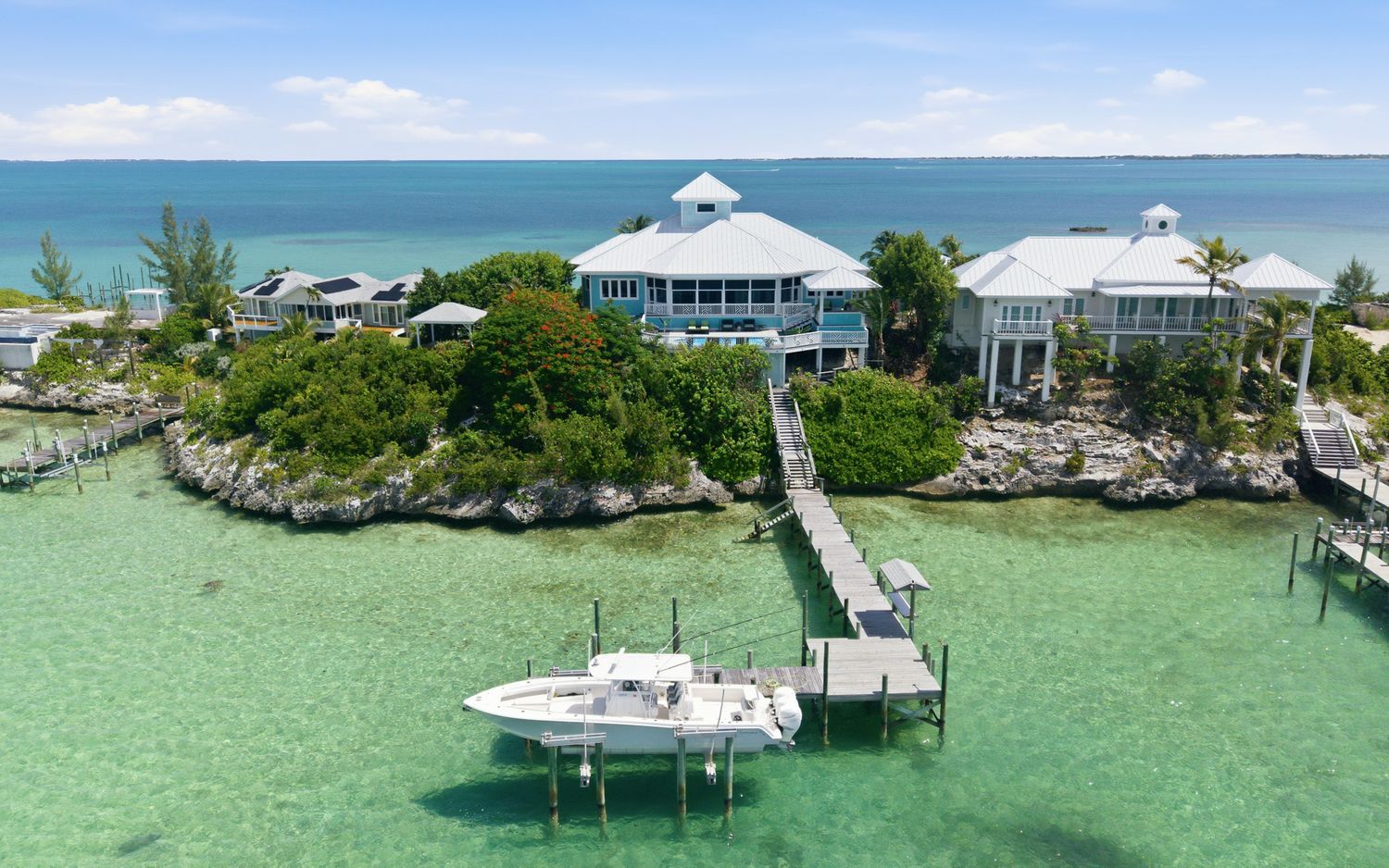 Aerial view of a luxury waterfront estate with a private dock and boat in crystal clear turquoise waters.