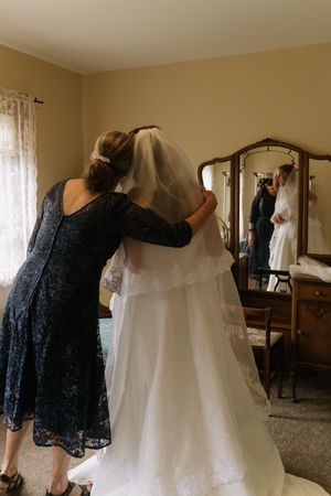 Mother helping bride with veil in bedroom mirror reflection on wedding day preparation.