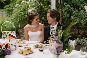 Bride and groom share a romantic glance at their outdoor wedding reception table surrounded by lush greenery.