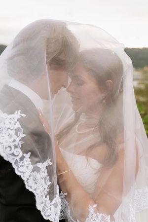 Romantic bride and groom share intimate moment under lace-trimmed wedding veil with soft natural light.