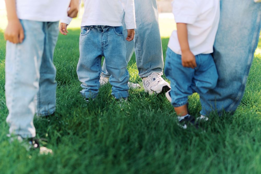 Group of children in blue jeans and white shirts playing with a soccer ball on green grass.