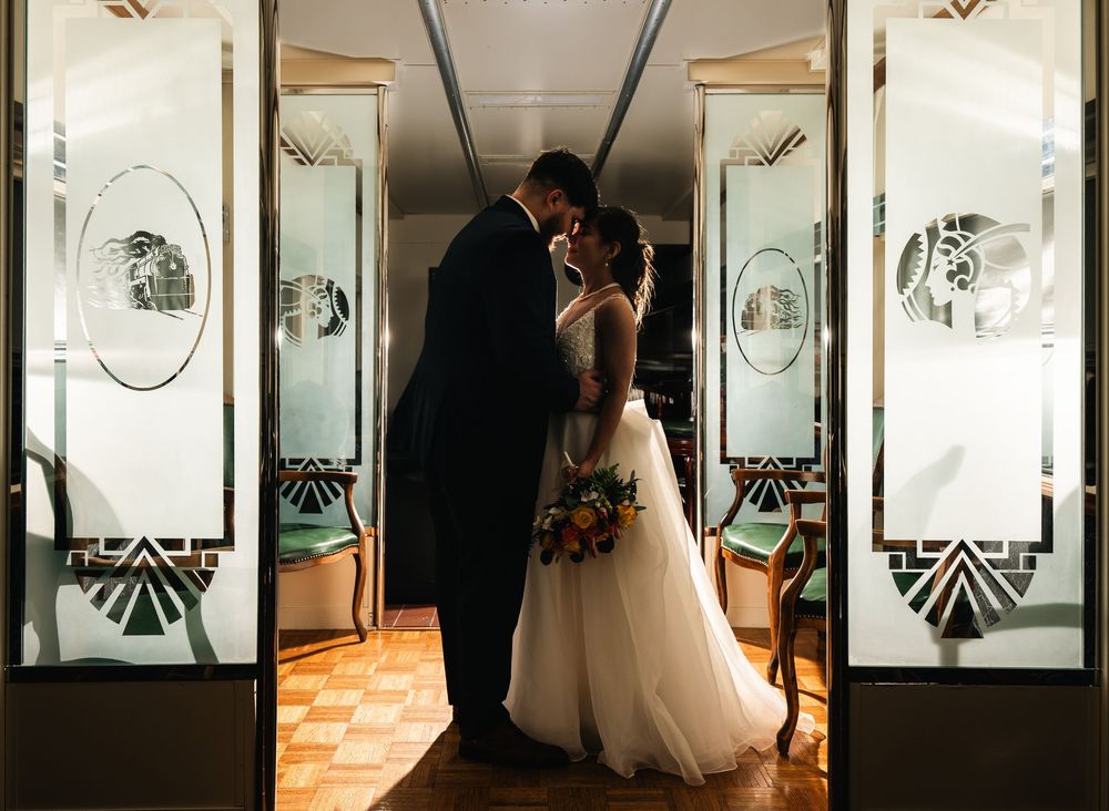 Newlyweds share a romantic kiss in an elegant Art Deco doorway with mirrored panels on their wedding day.