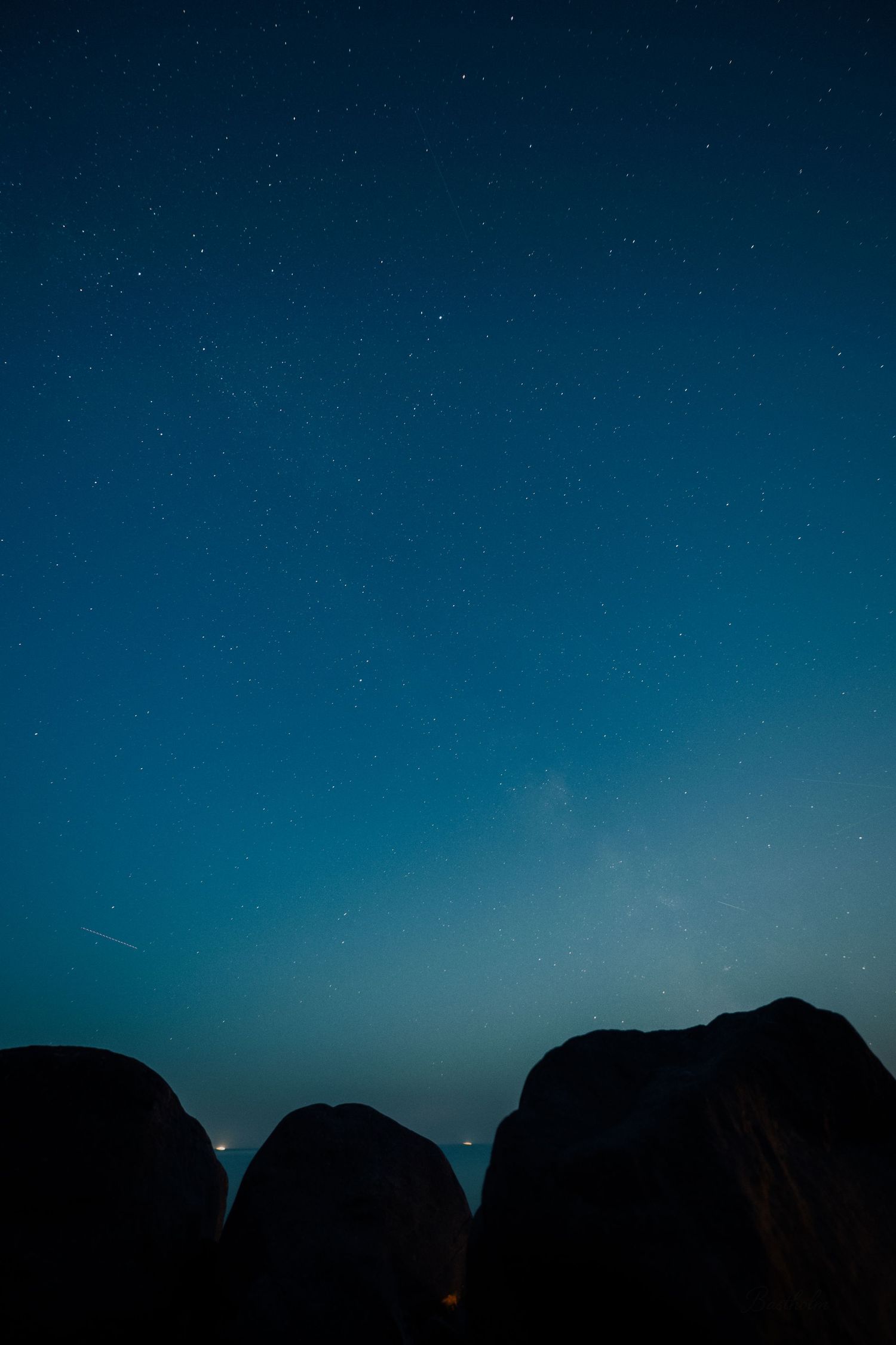 A stunning night sky filled with stars above dark silhouetted rock formations under a deep blue gradient.
