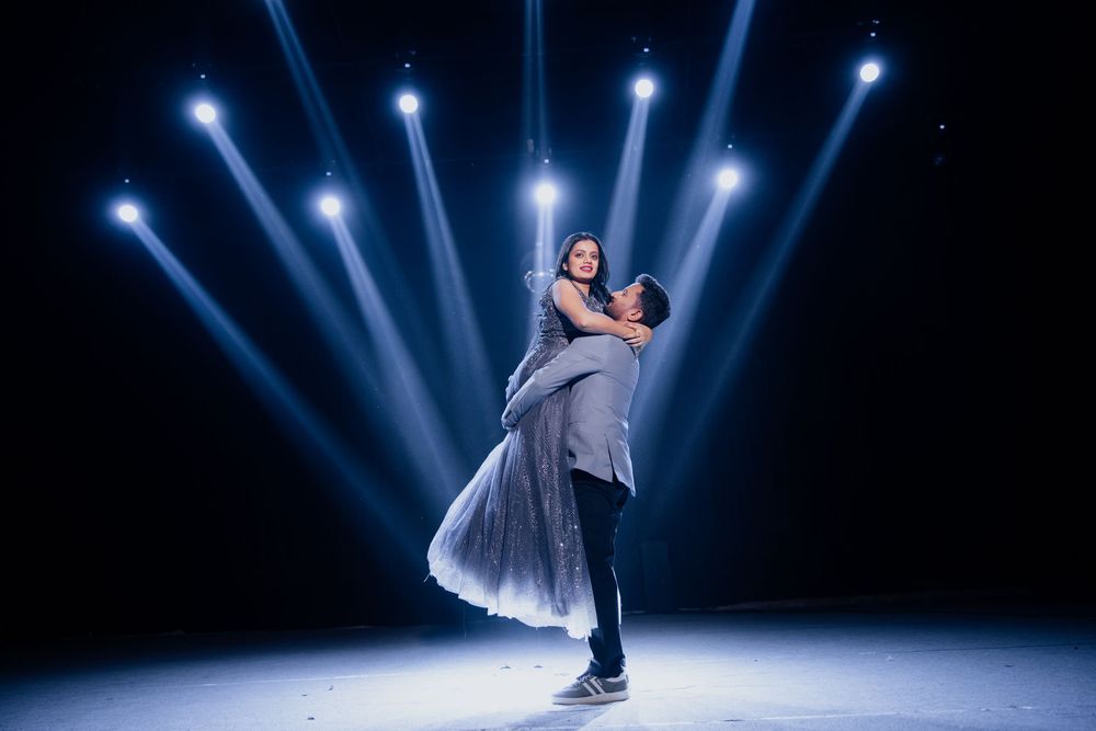 Two dancers perform a romantic lift on a dramatic stage with blue spotlights shining behind them.