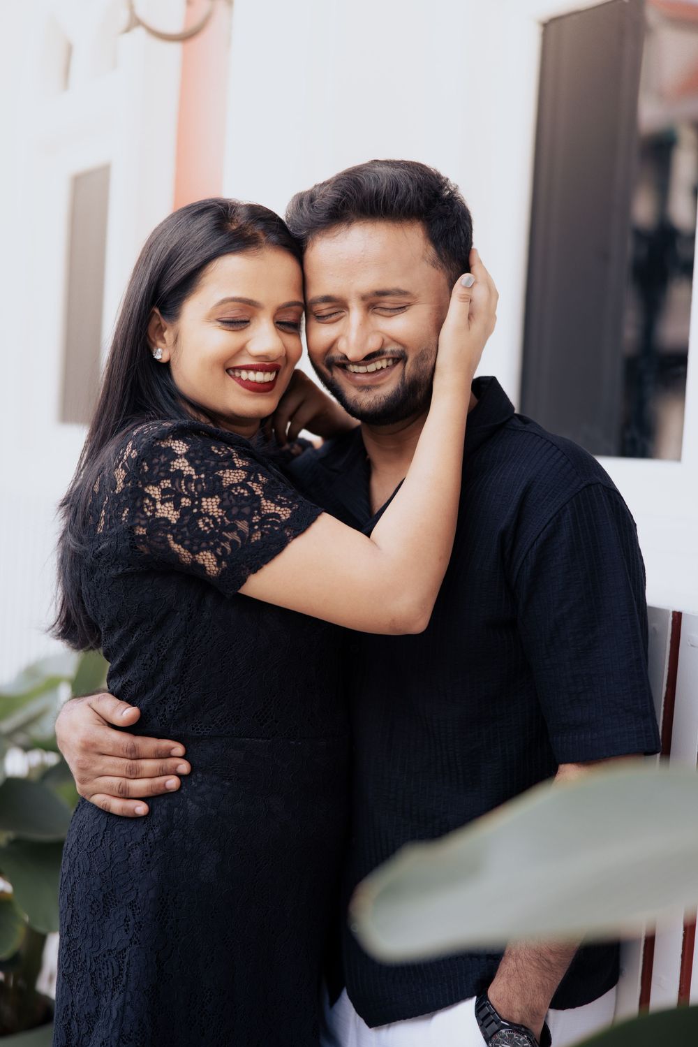 Happy Indian couple in black outfits sharing a warm embrace, smiling joyfully in an outdoor setting.