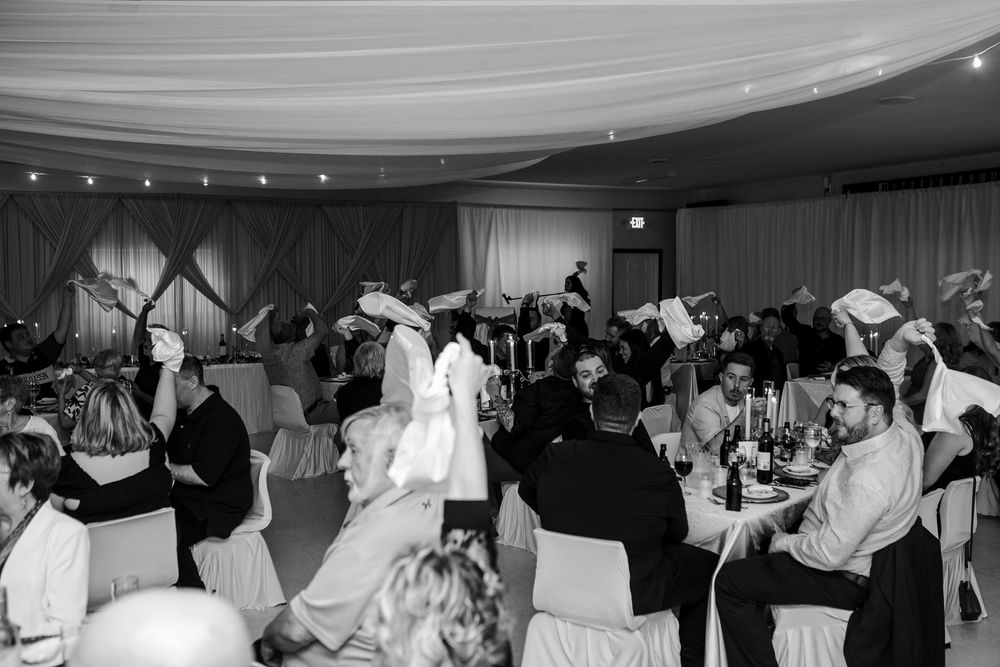Black and white photo of guests dancing and celebrating at an elegant wedding reception in a decorated banquet hall.