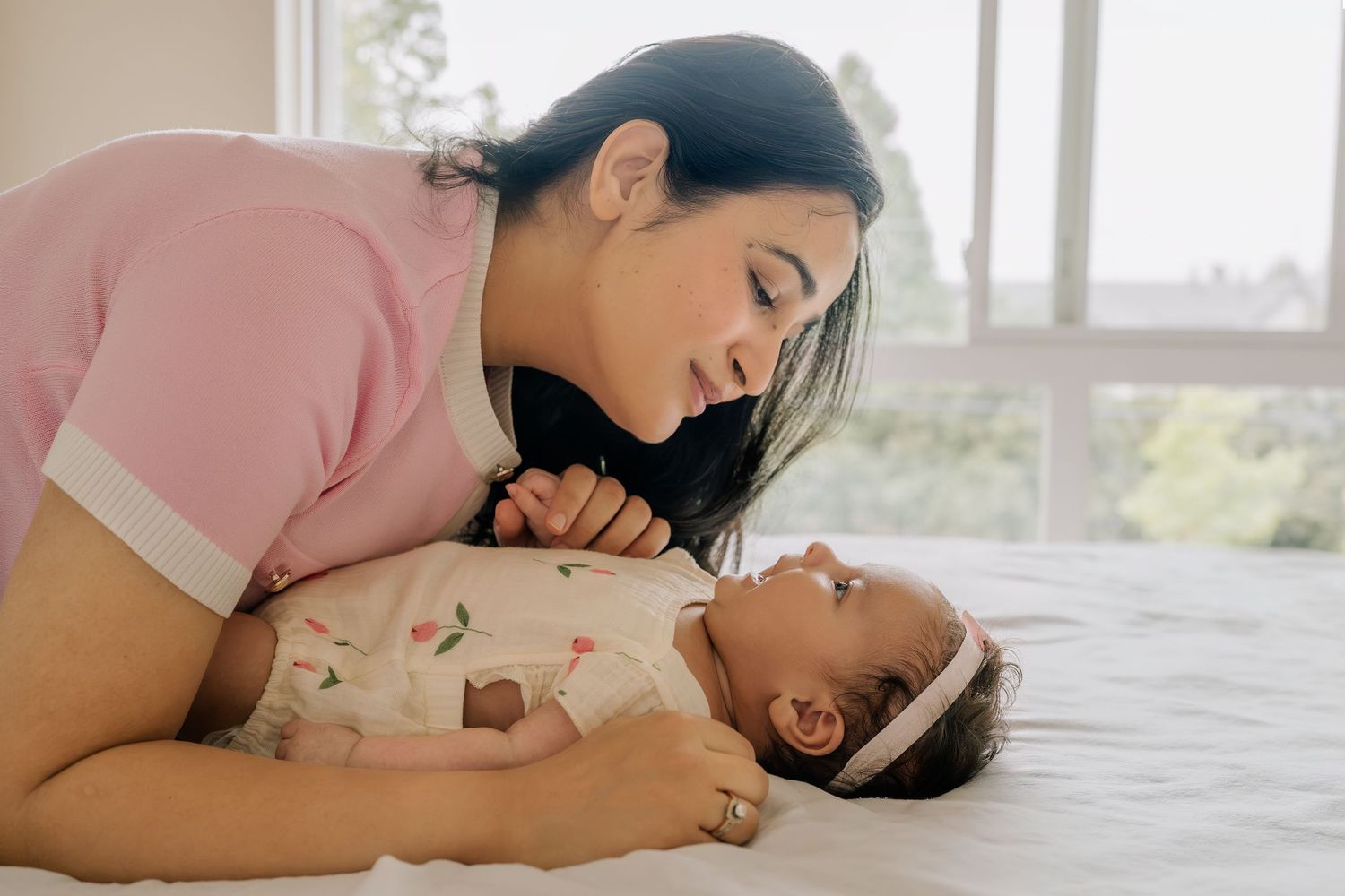 A loving mother leaning over her newborn baby lying on a white bed, sharing a tender bonding moment.