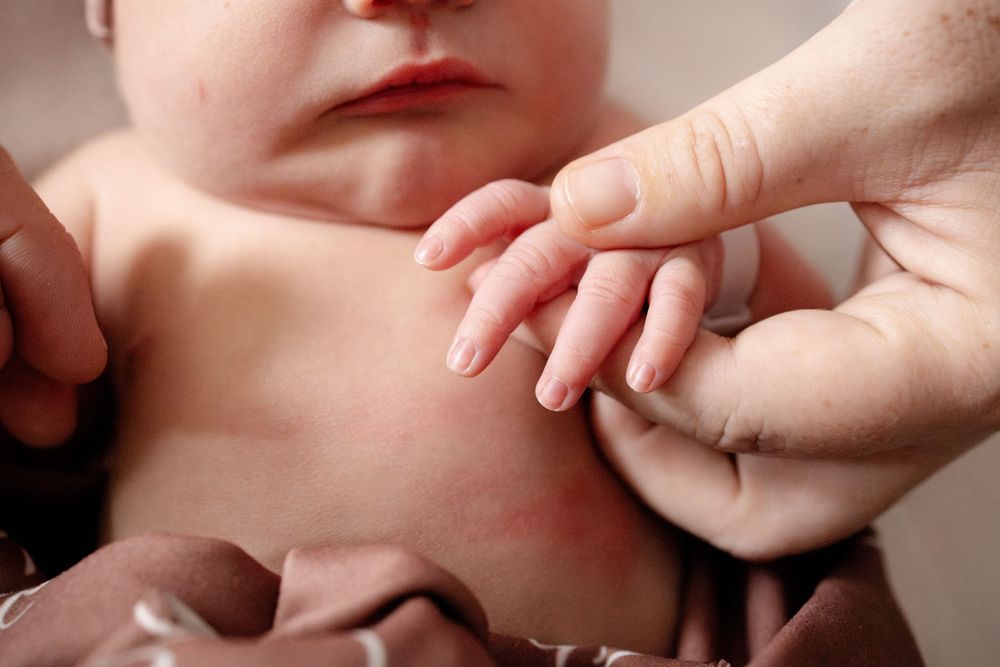Close-up of a parent's hand gently holding the tiny fingers of a newborn baby during a Fresh 48 session at Parkwest Medical Center.