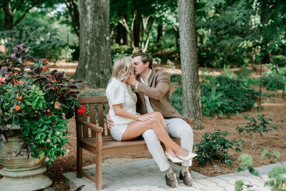 Couple sitting closely on a wooden garden bench surrounded by lush greenery and flowers.