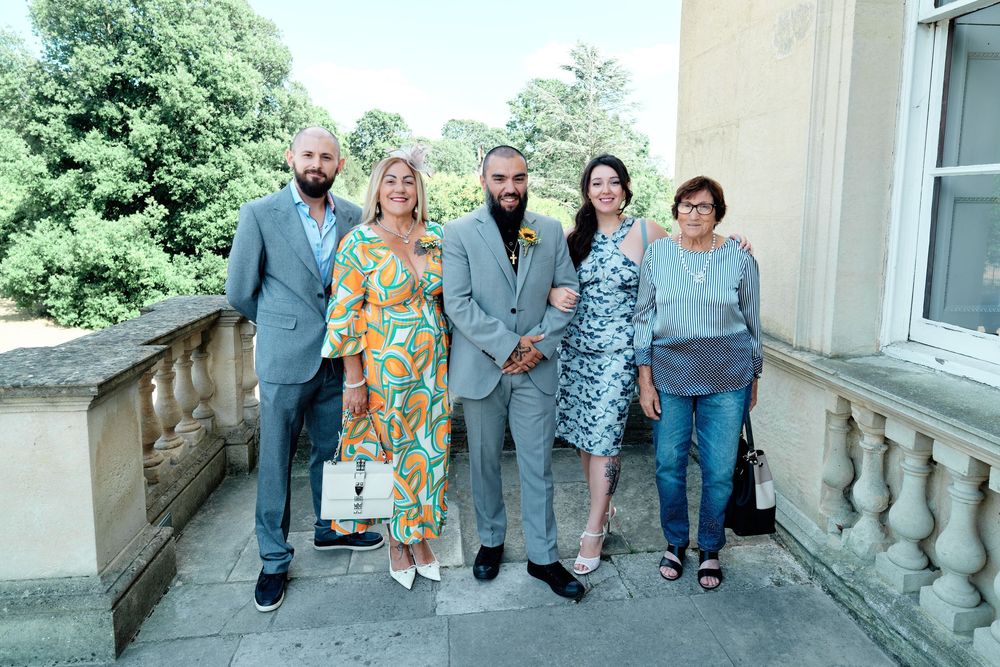 Five adults posing together outdoors near a classical stone balustrade on a sunny day.