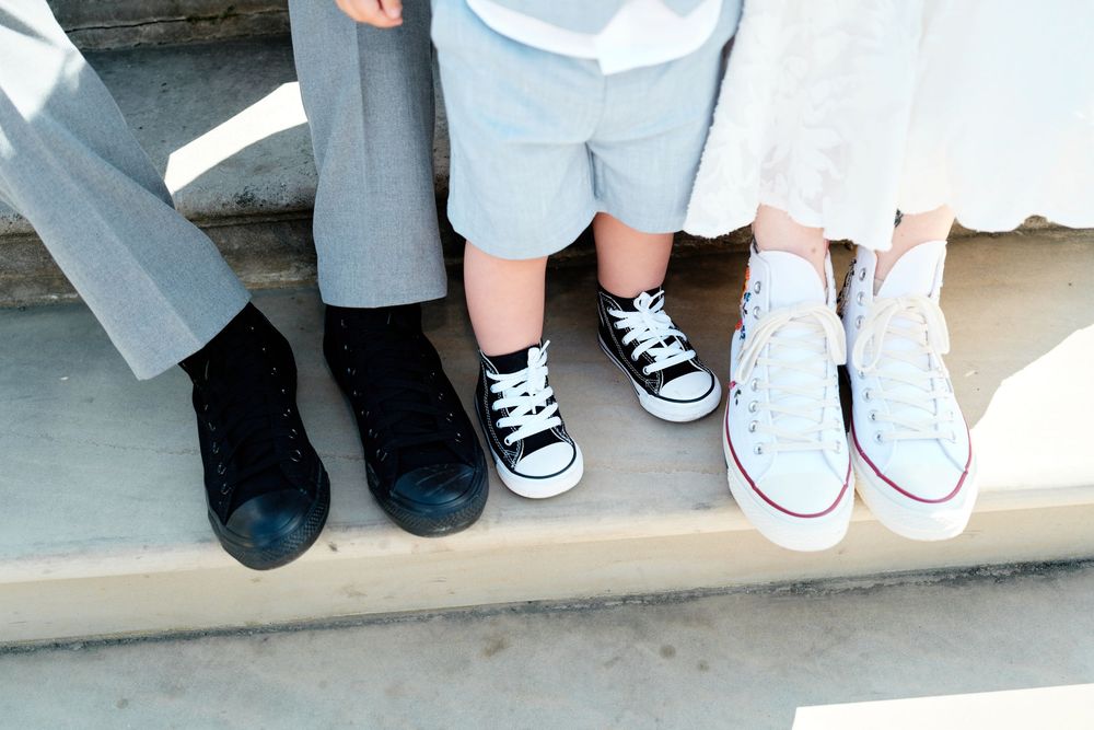 Three people sitting on steps wearing Converse sneakers, including black, black-and-white, and white high-tops.