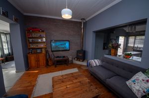 Cozy living room with a gray sofa, rustic wooden coffee table, brick accent wall, wood burning stove, flat-screen TV and hardwood floors.