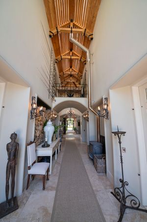 Elegant long hallway with vaulted wood-beam ceiling, stone tile floor, runner rug, wrought iron candle stand, and decorative console table.