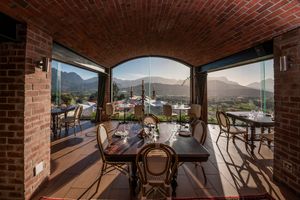Elegant dining table with wooden chairs under a brick vaulted ceiling, with floor-to-ceiling glass doors framing a scenic mountain view.