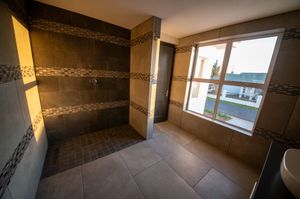 Spacious walk-in tiled shower with dark stone-look walls and mosaic accent bands beside a large window overlooking a neighborhood.