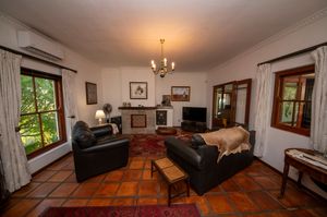 Cozy living room with terracotta tile floors, black leather sofas, a rustic wooden coffee table, chandelier and a brick fireplace.