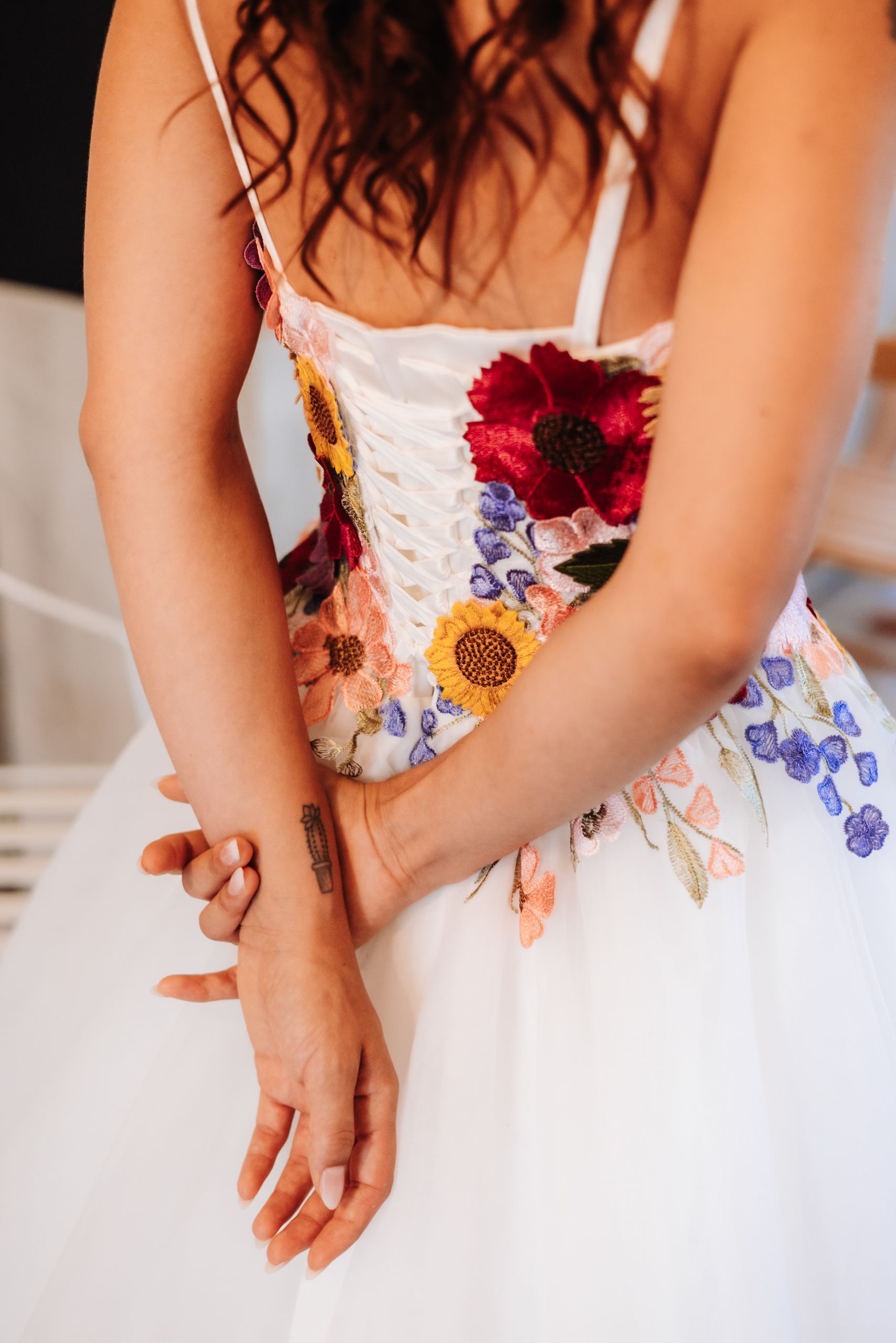 Bride in white floral embroidered wedding dress with colorful flowers detail.