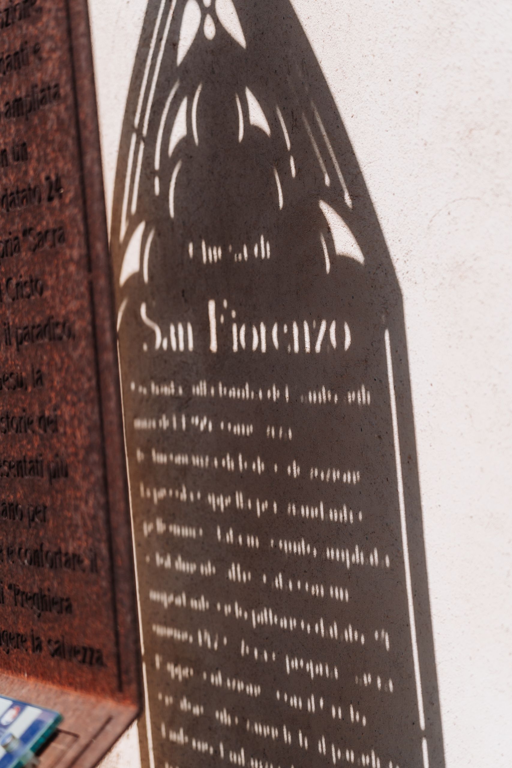 Metal sign for Chiesa di San Fiorenzo church with decorative Gothic arch cutout design mounted on a wall.