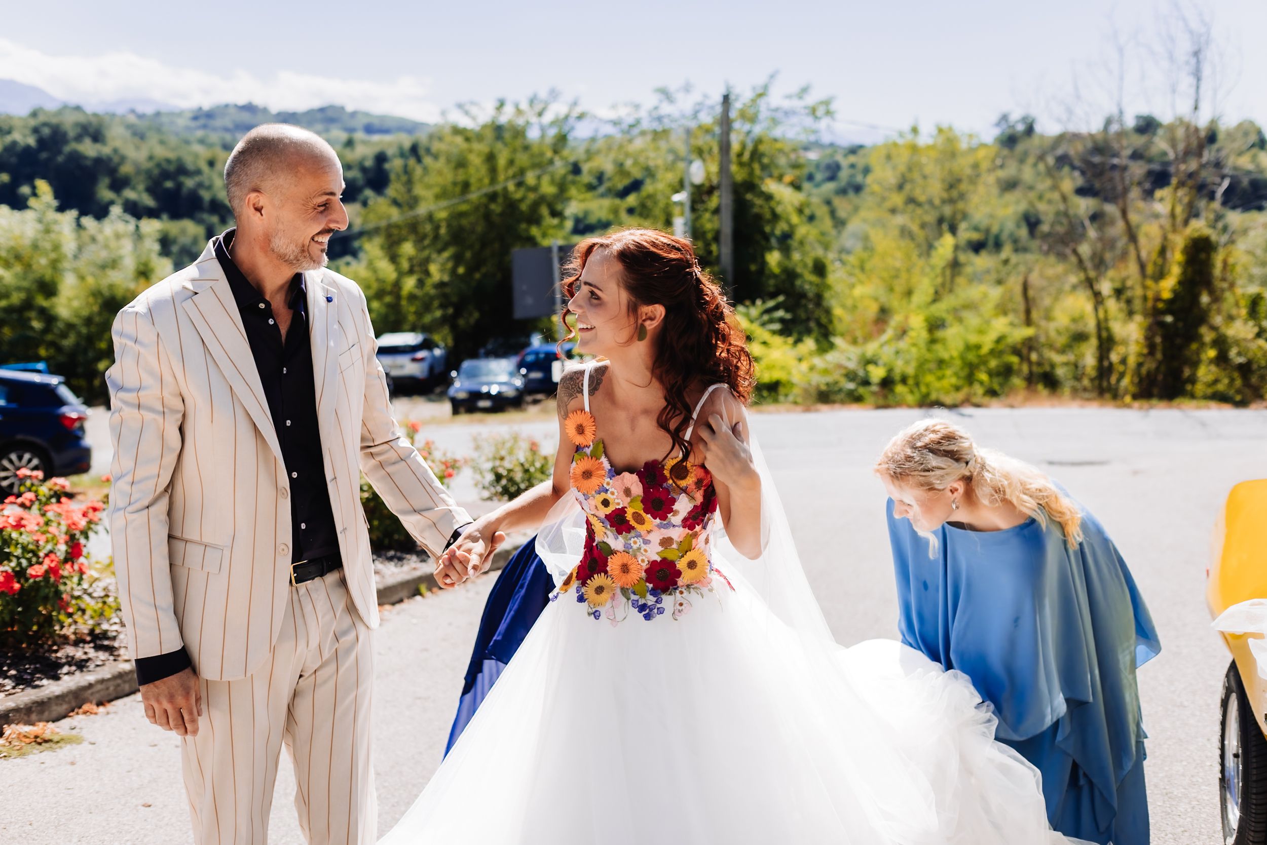 Bride in blue tulle gown holding colorful bouquet laughs with groom in striped suit at outdoor wedding ceremony.