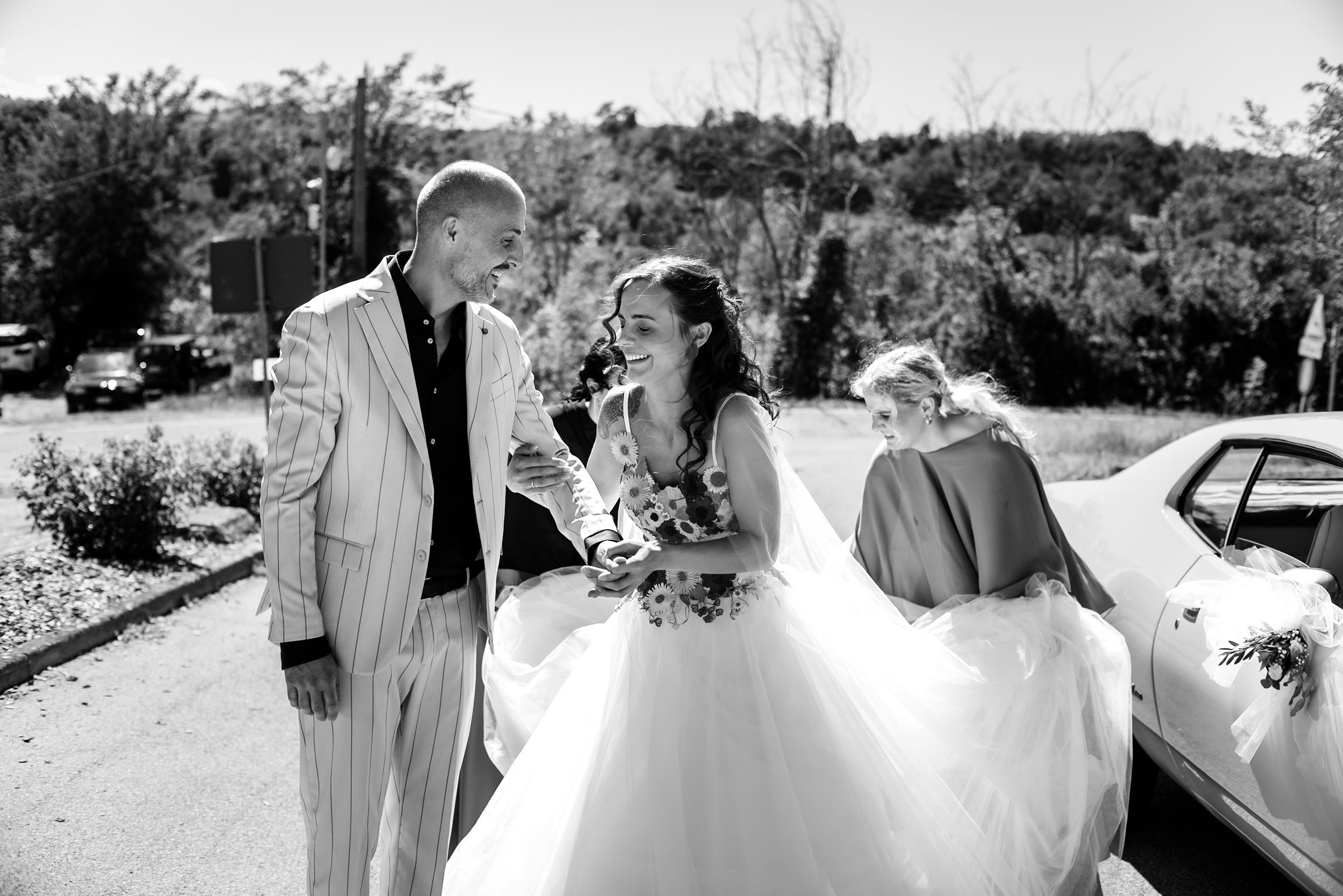Black and white photo of a bride in a white gown laughing with a groom in a striped suit outdoors.