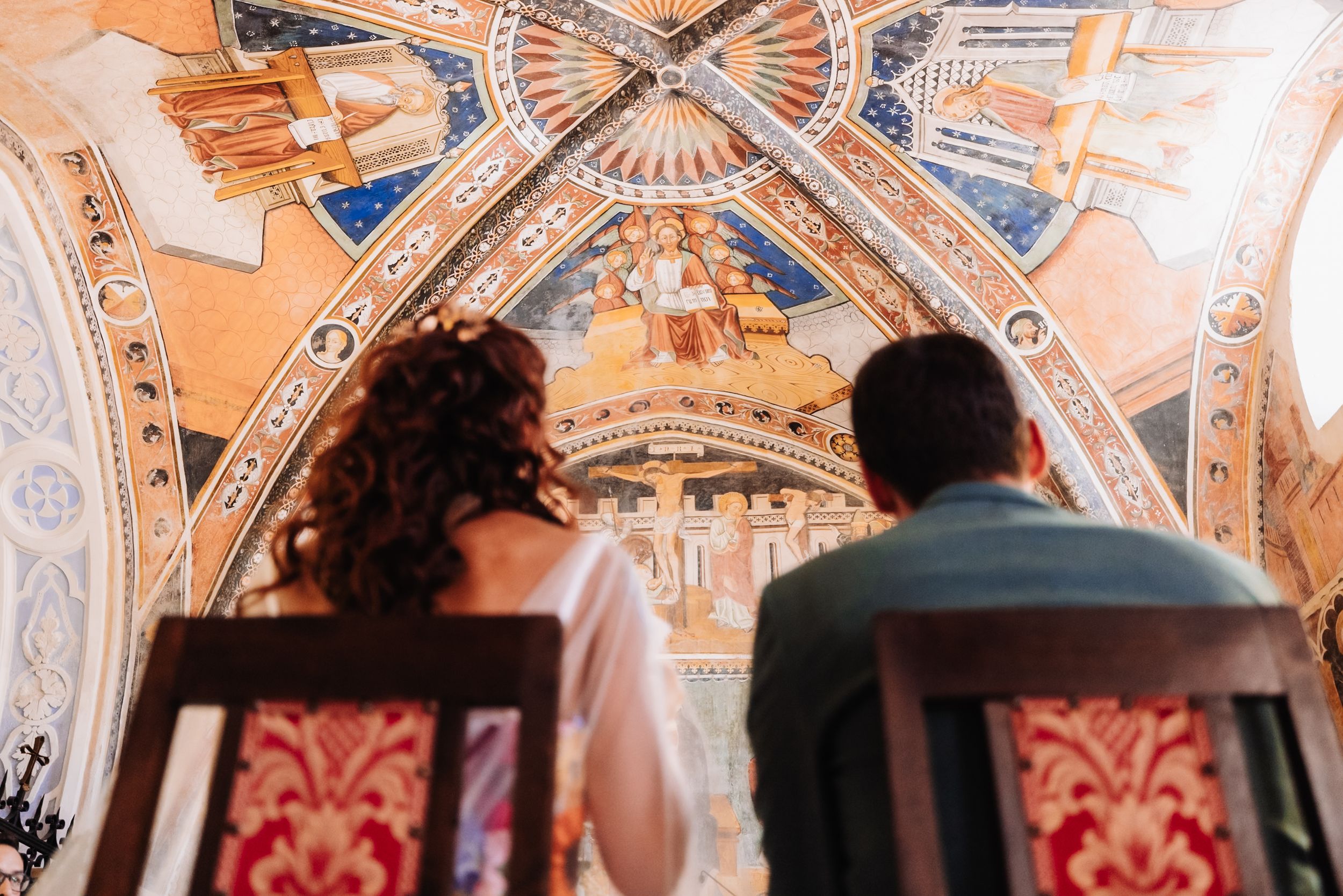 Couple seated in ornate chairs admiring stunning Byzantine fresco ceiling artwork in a historic chapel.