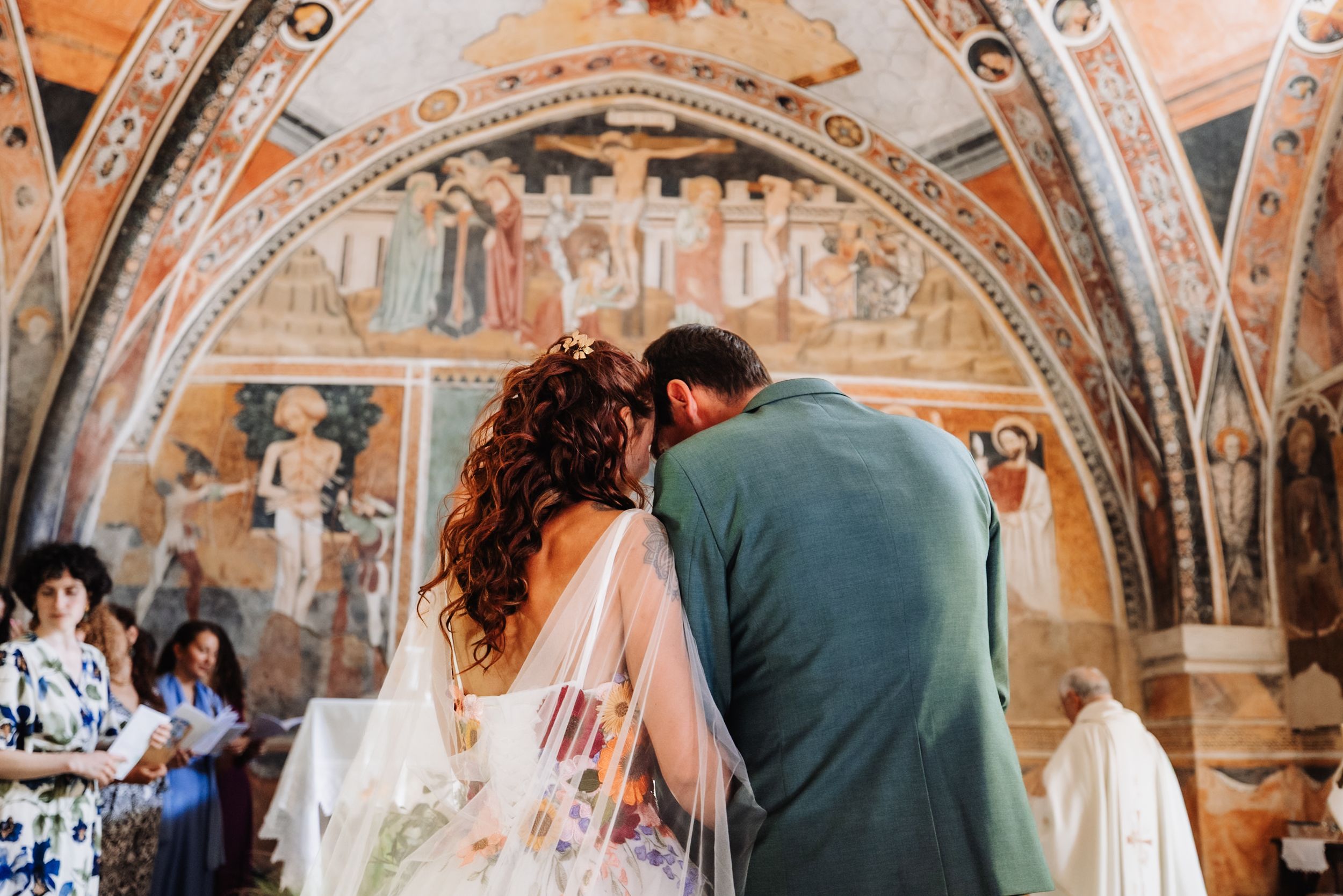 Bride and groom share an intimate moment in a stunning Italian chapel adorned with ancient frescoes during their wedding ceremony.