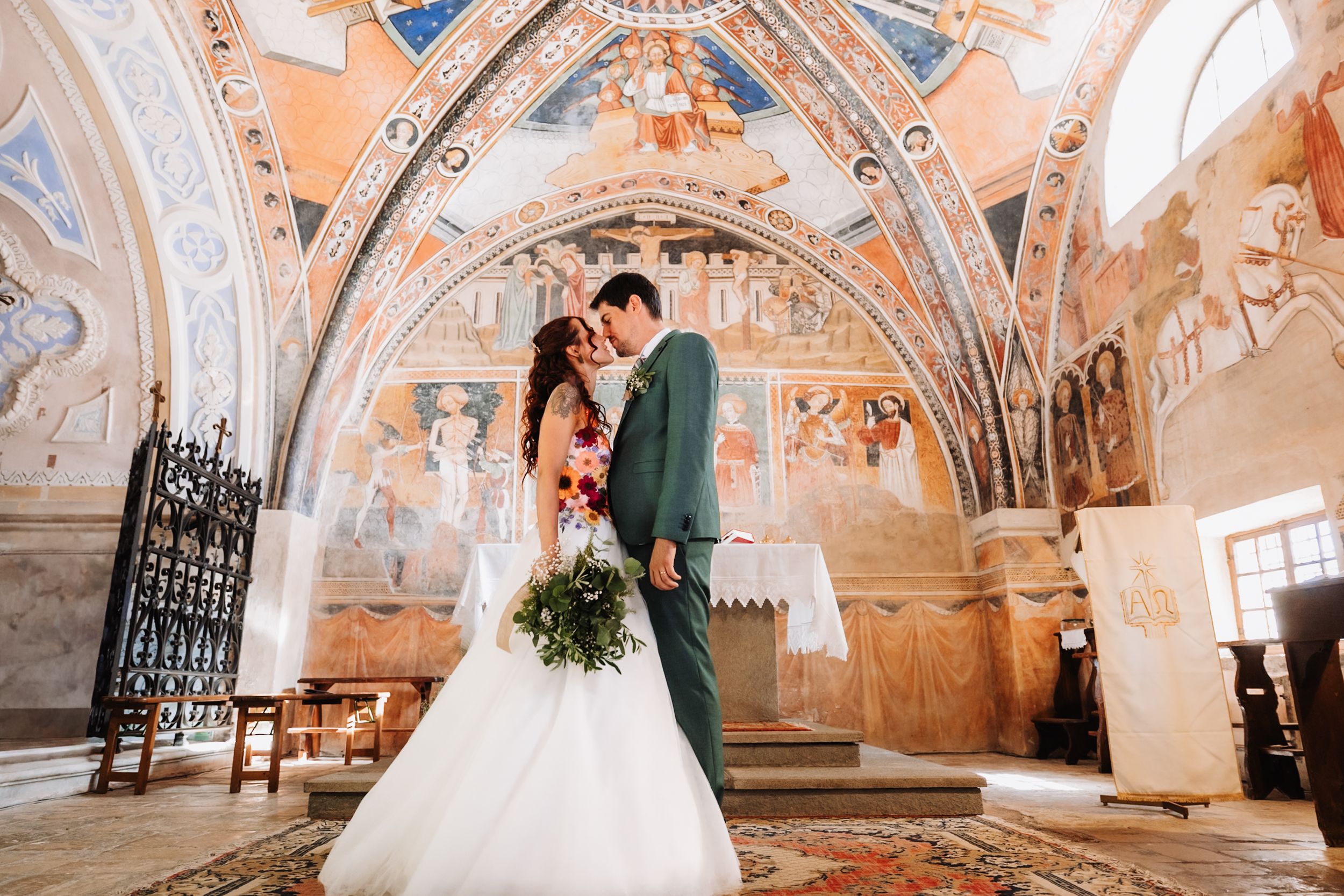 Bride and groom share a romantic moment in an ornate chapel with stunning frescoes and arched ceilings.