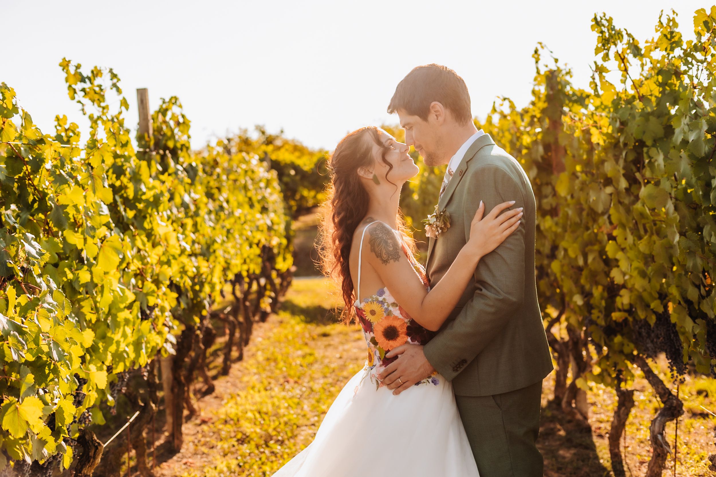 Bride and groom embracing in a sunlit vineyard, sharing a romantic moment in wedding attire.