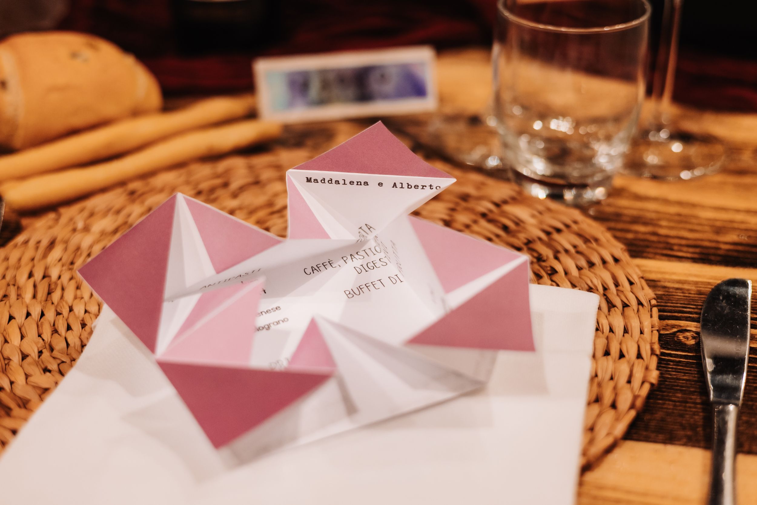 Pink and white origami fortune teller wedding place card on woven placemat at elegant table setting.