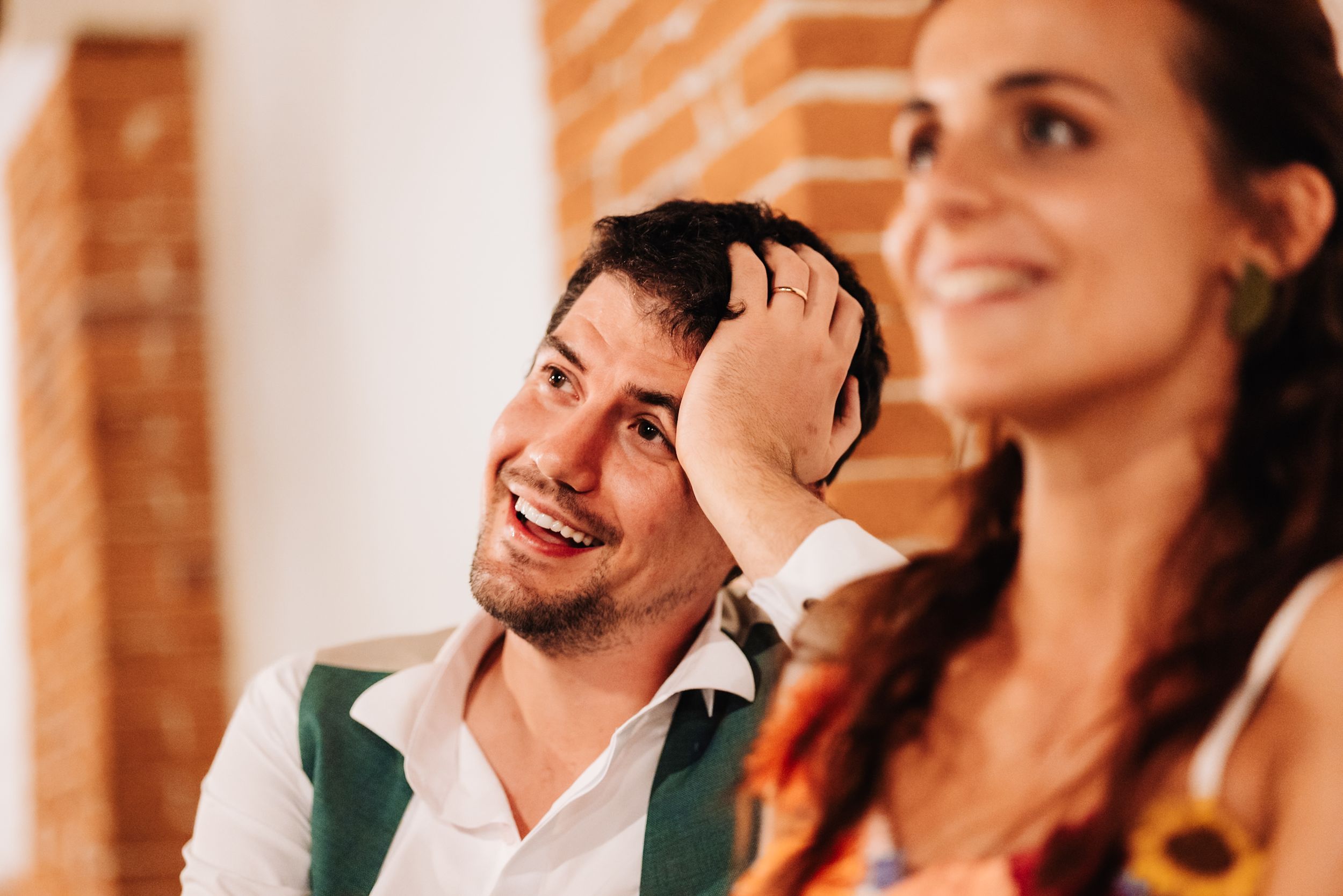 Happy couple laughing at a wedding, man in white shirt with hand on head, woman with sunflower dress.