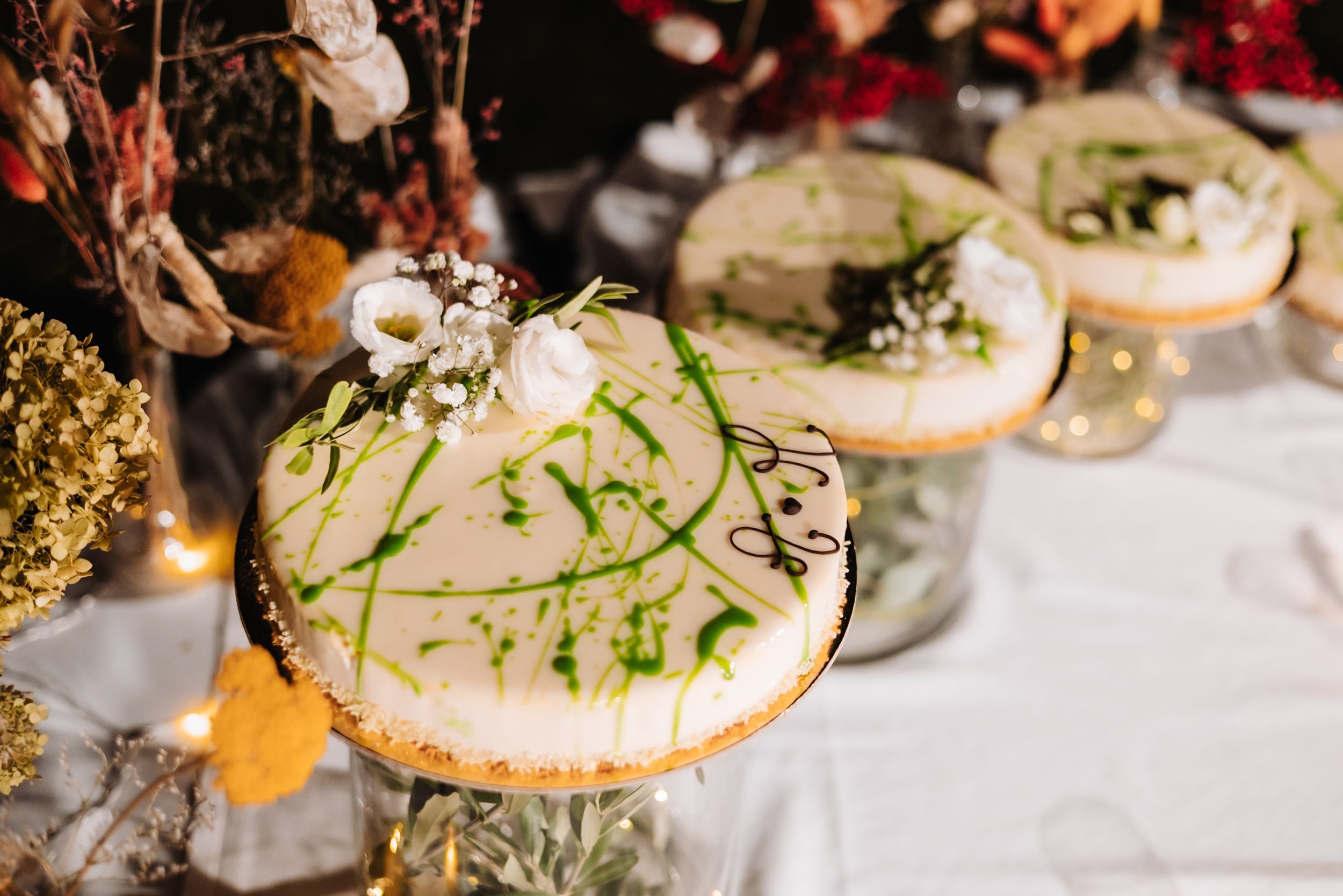 Elegant wedding cheesecakes decorated with green botanical designs and white flowers displayed on glass cake stands.
