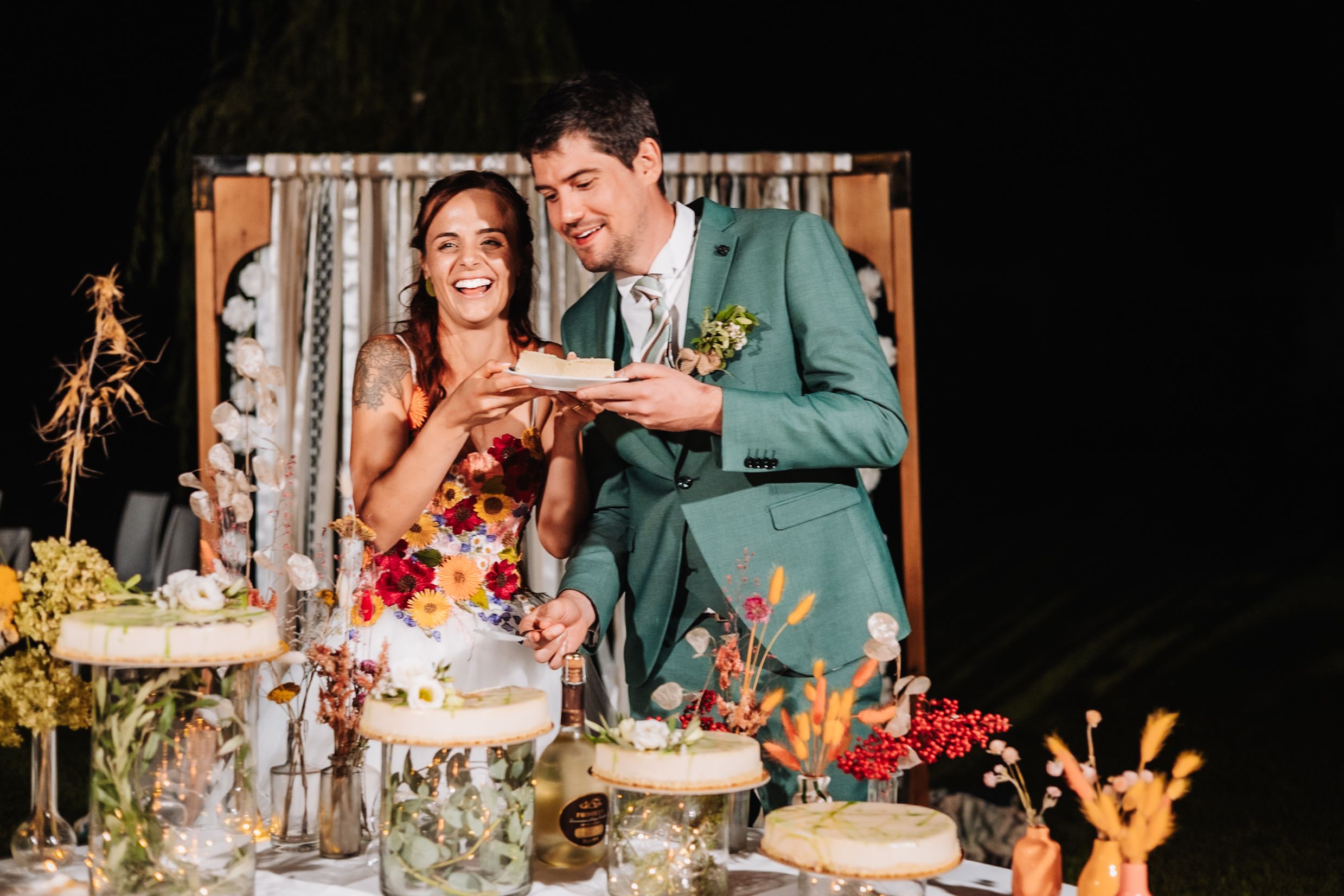 Bride and groom smiling while cutting their wedding cake at an elegant outdoor night reception.