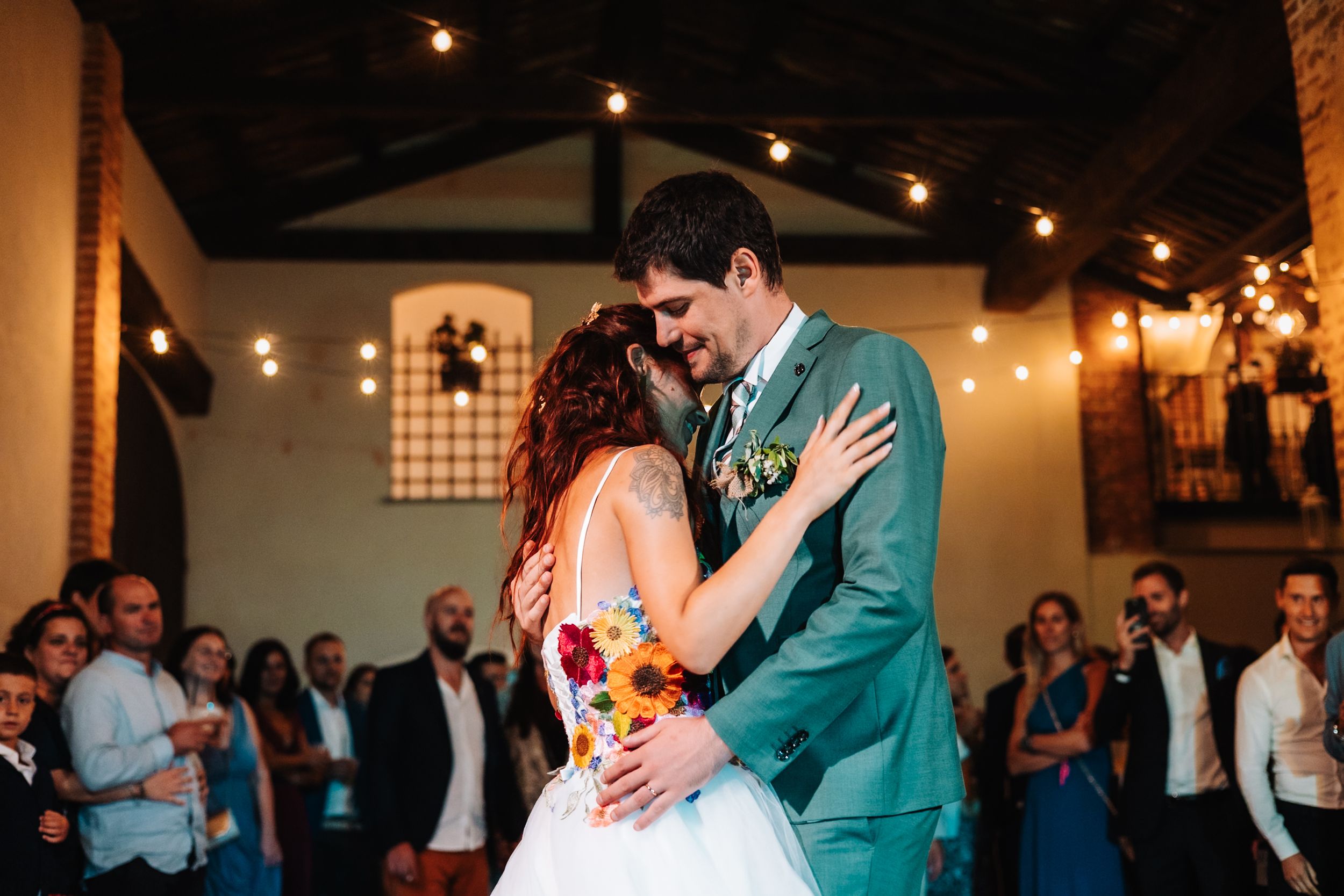 Bride and groom share first dance under string lights at rustic wedding reception venue.