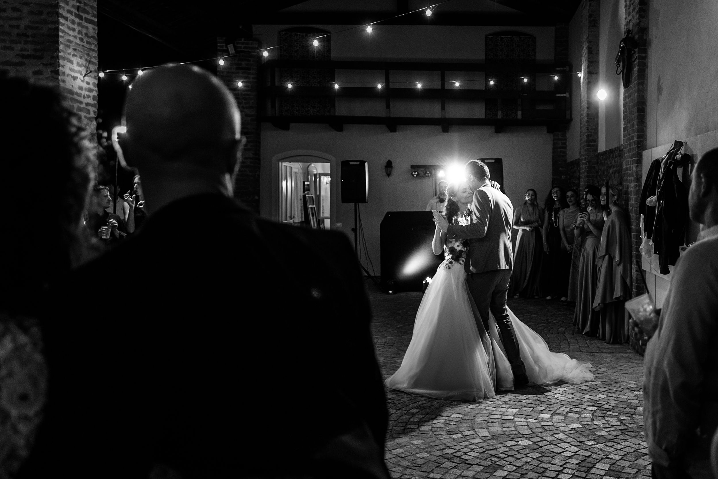 Black and white photo of bride and groom sharing first dance at elegant wedding reception with string lights.