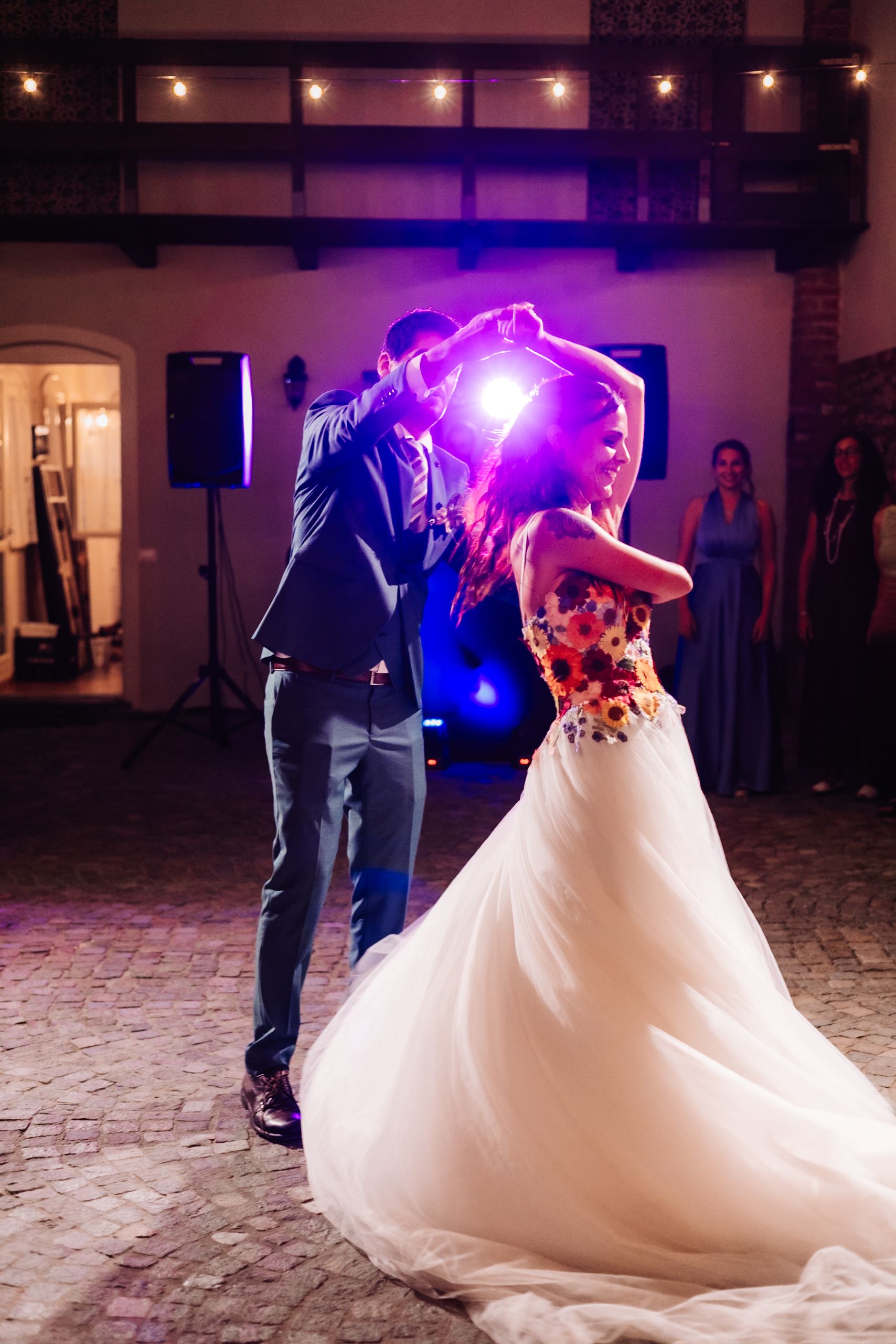 Bride and groom share their first dance at a wedding reception, illuminated by colorful lights.