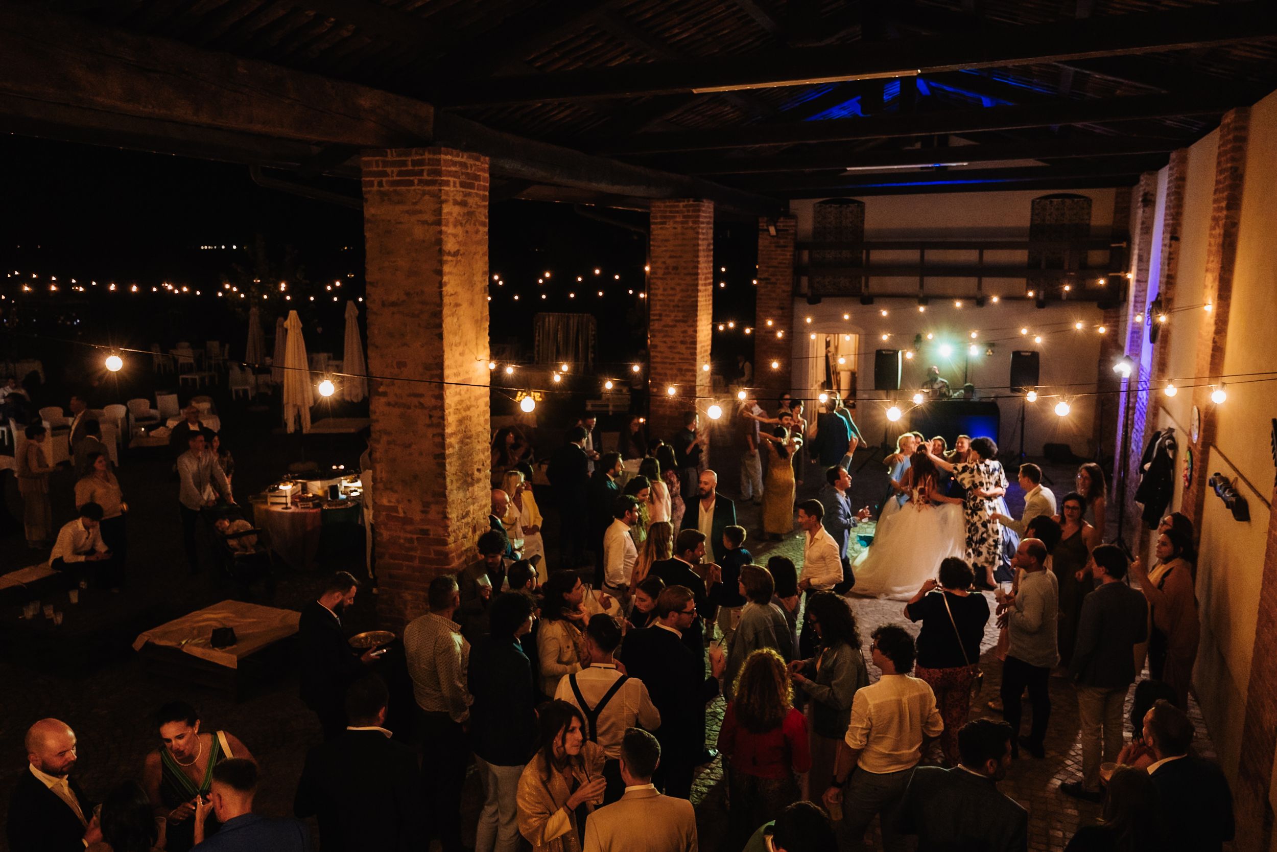 Elegant indoor event venue with string lights, brick columns, and guests mingling on a dance floor at night.