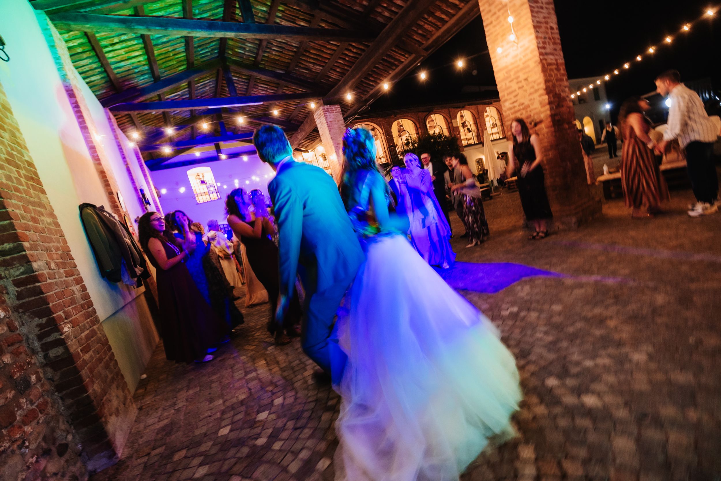 Bride and groom share first dance at elegant outdoor wedding reception with string lights and brick arches.