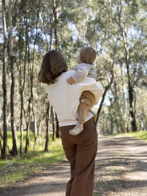 Mother holding baby while walking on a forest path surrounded by tall eucalyptus trees.