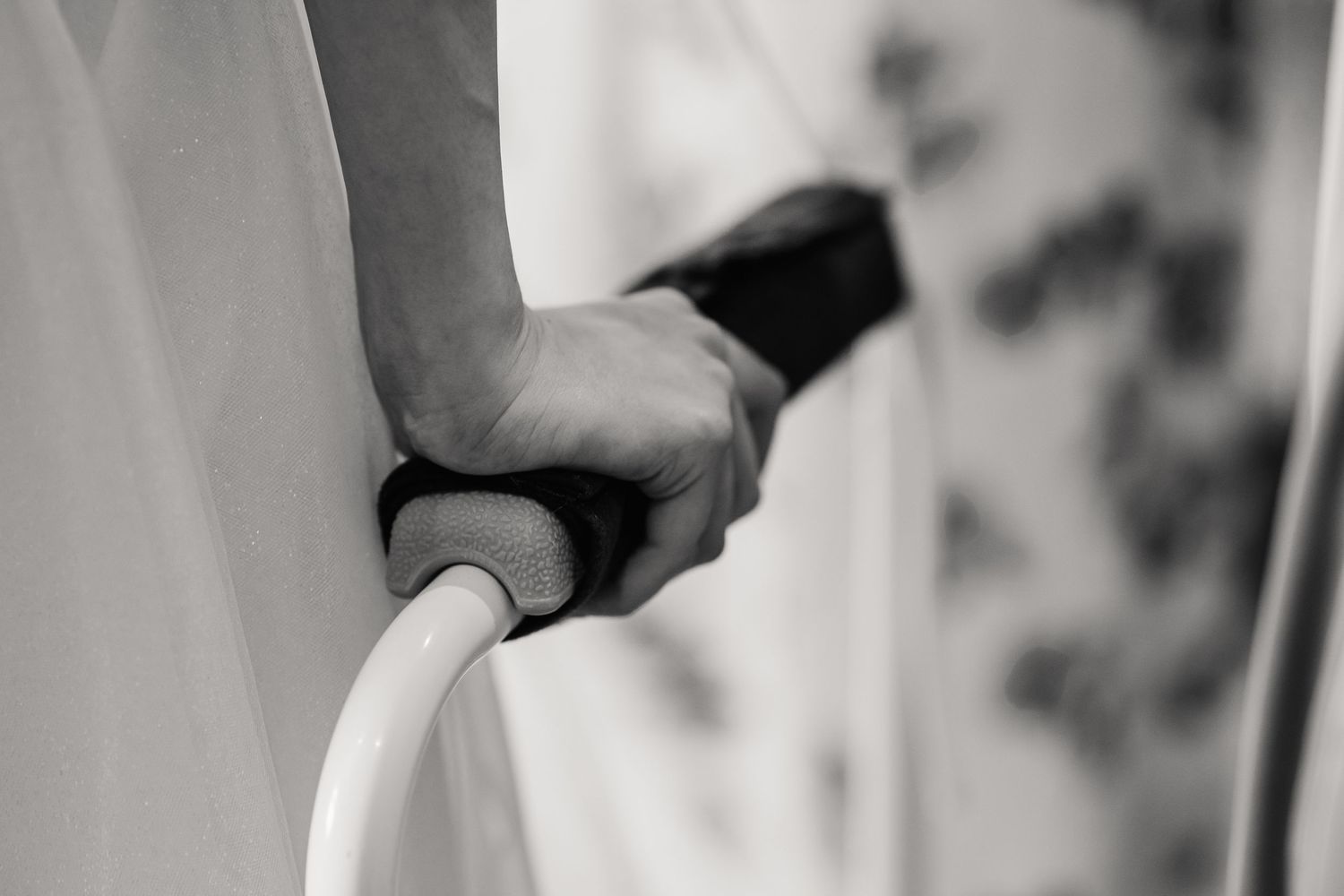 Black and white close-up of an elderly person's hand gripping a padded walker handle, symbolizing mobility support and senior care.