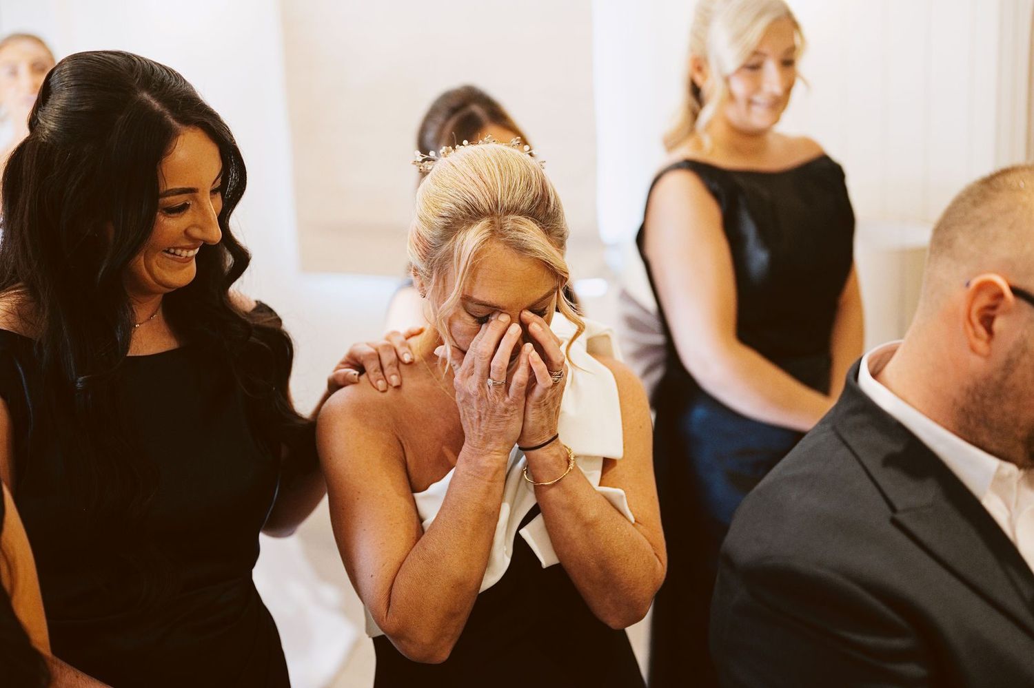 Guest in a black and white dress wiping away tears as friends smile beside her, Sandhole Oak Barn wedding